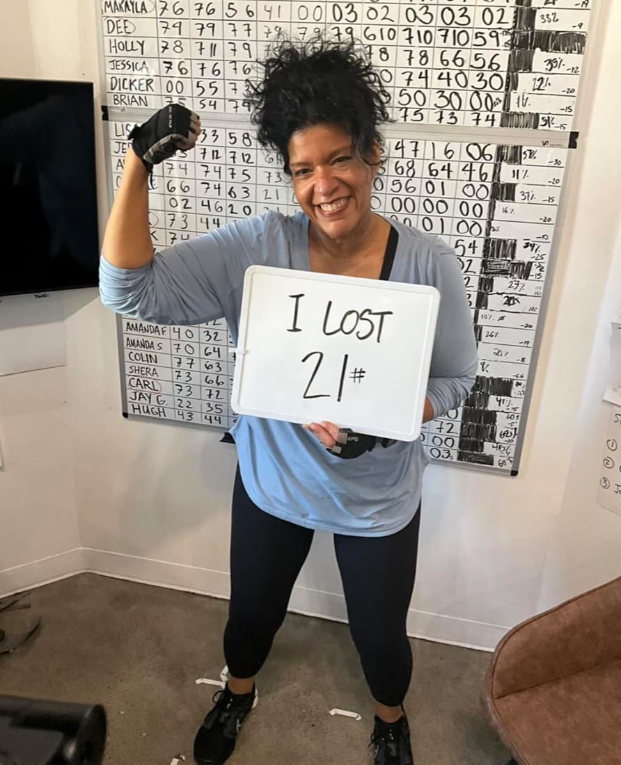 Leaner Fitness member holding a sign reading I lost 21 lbs